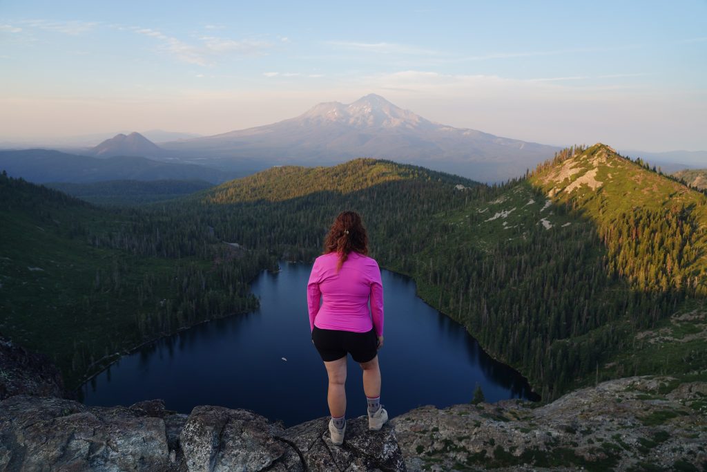 Hiker overlooking a heart shaped lake and Mount Shasta at sunset.