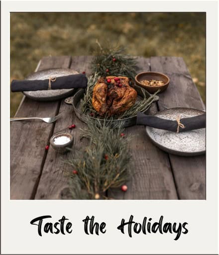 Polaroid with Thanksgiving meal, plates, and silverware served on a table outside with "Taste the Holidays" written on it.