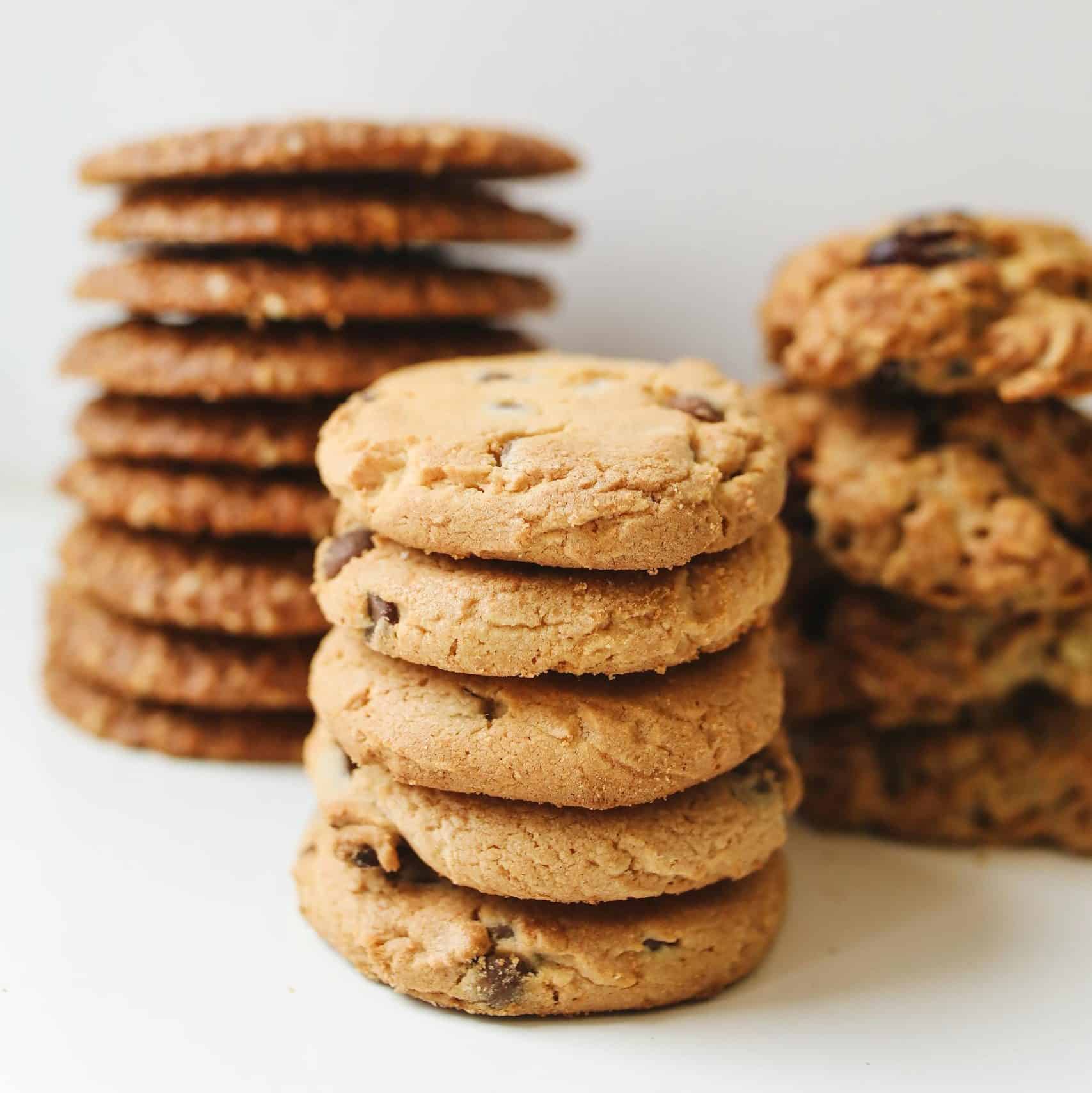 A variety of delicious homemade cookies stacked neatly in piles on a white background.