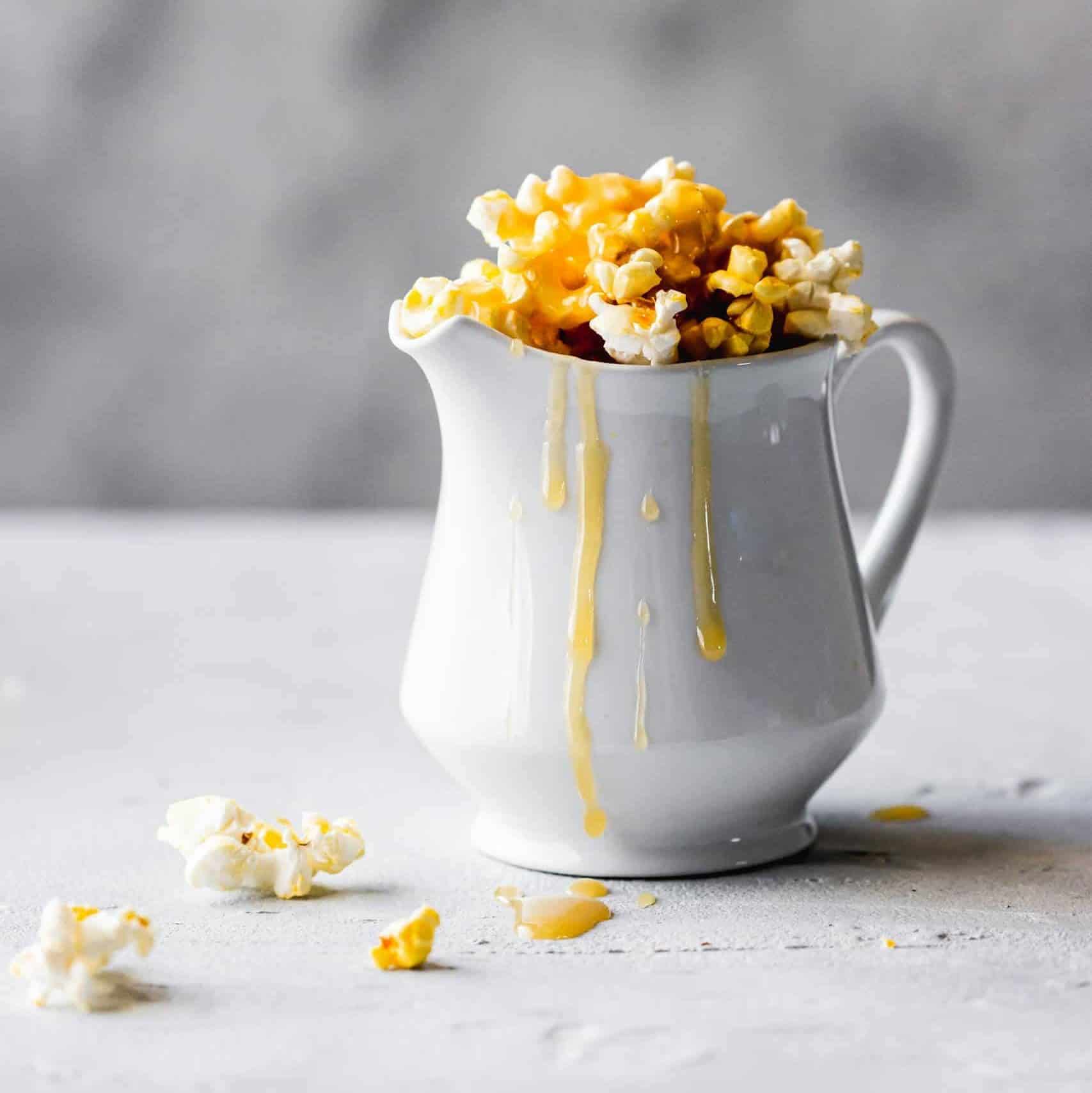 Delicious caramel popcorn spilling from a white jug, artistic food display.
