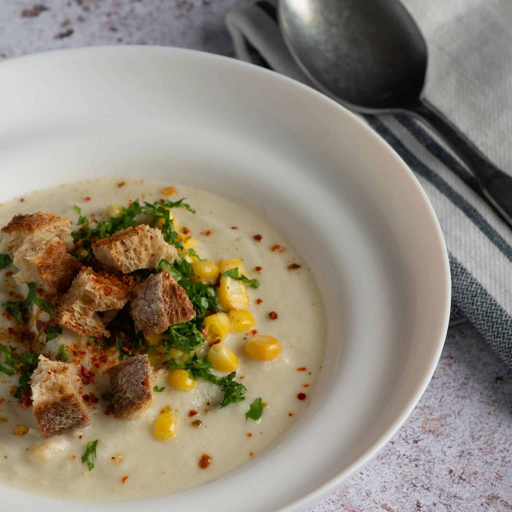 Delicious creamy corn chowder topped with fresh croutons and parsley in a white bowl.