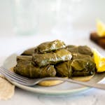 Close-up of traditional Greek dolmades on a plate with lemon wedges and a fork.