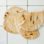 Overhead view of fresh pita bread on a white tiled background, perfect for food styling and recipe use.