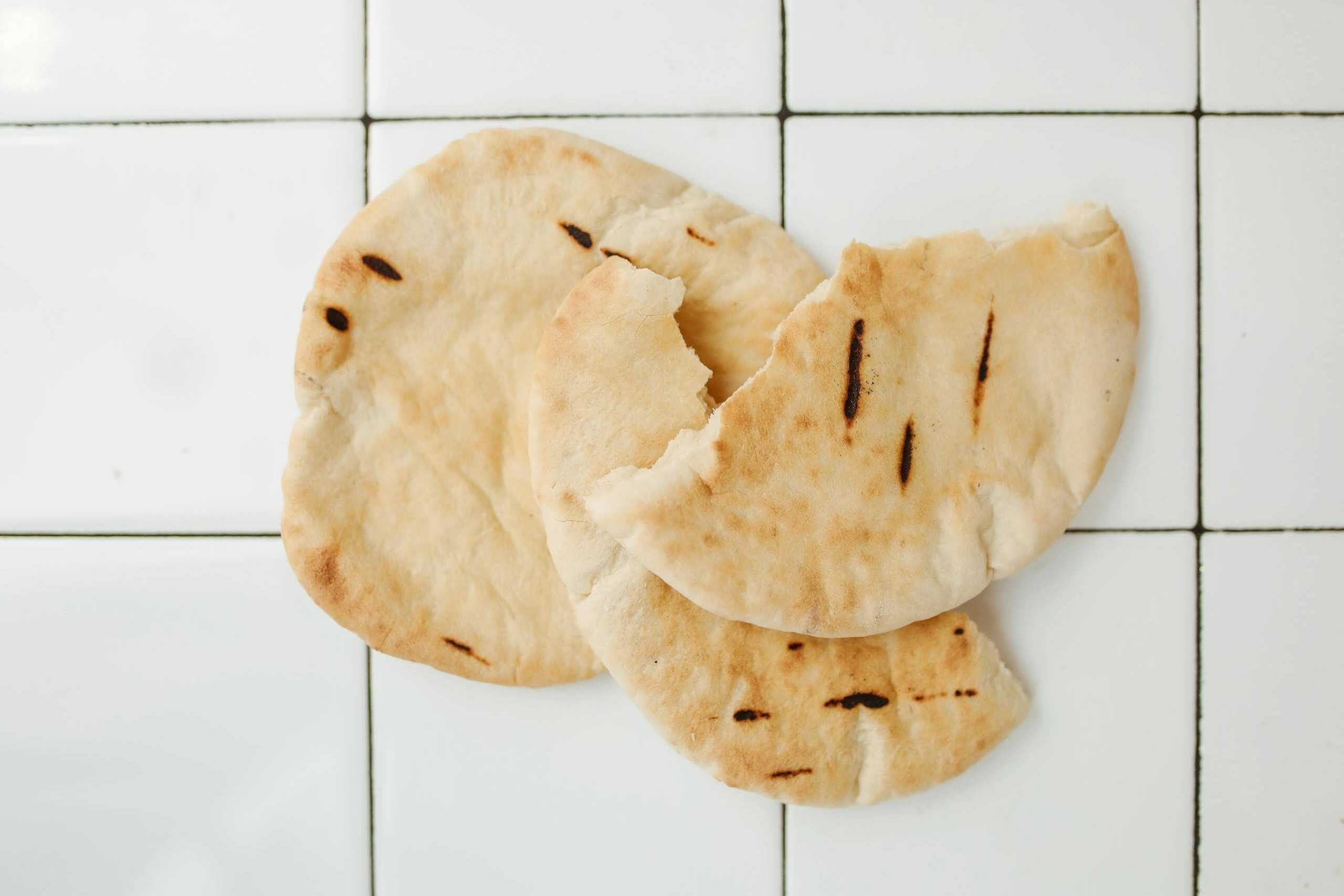 Overhead view of fresh pita bread on a white tiled background, perfect for food styling and recipe use.