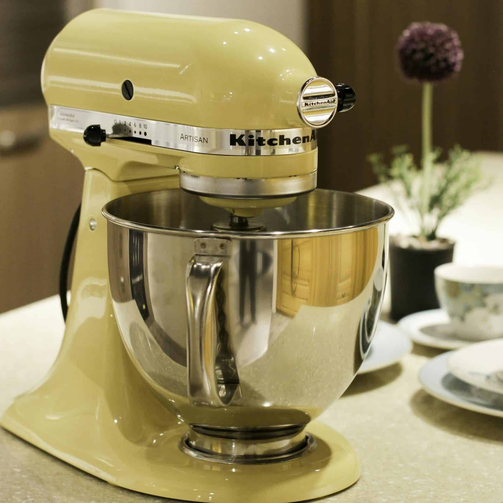 Vibrant yellow stand mixer on a kitchen countertop beside tableware and decor.