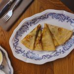 Tasty crepes beautifully plated on ornate porcelain with syrup and cutlery.