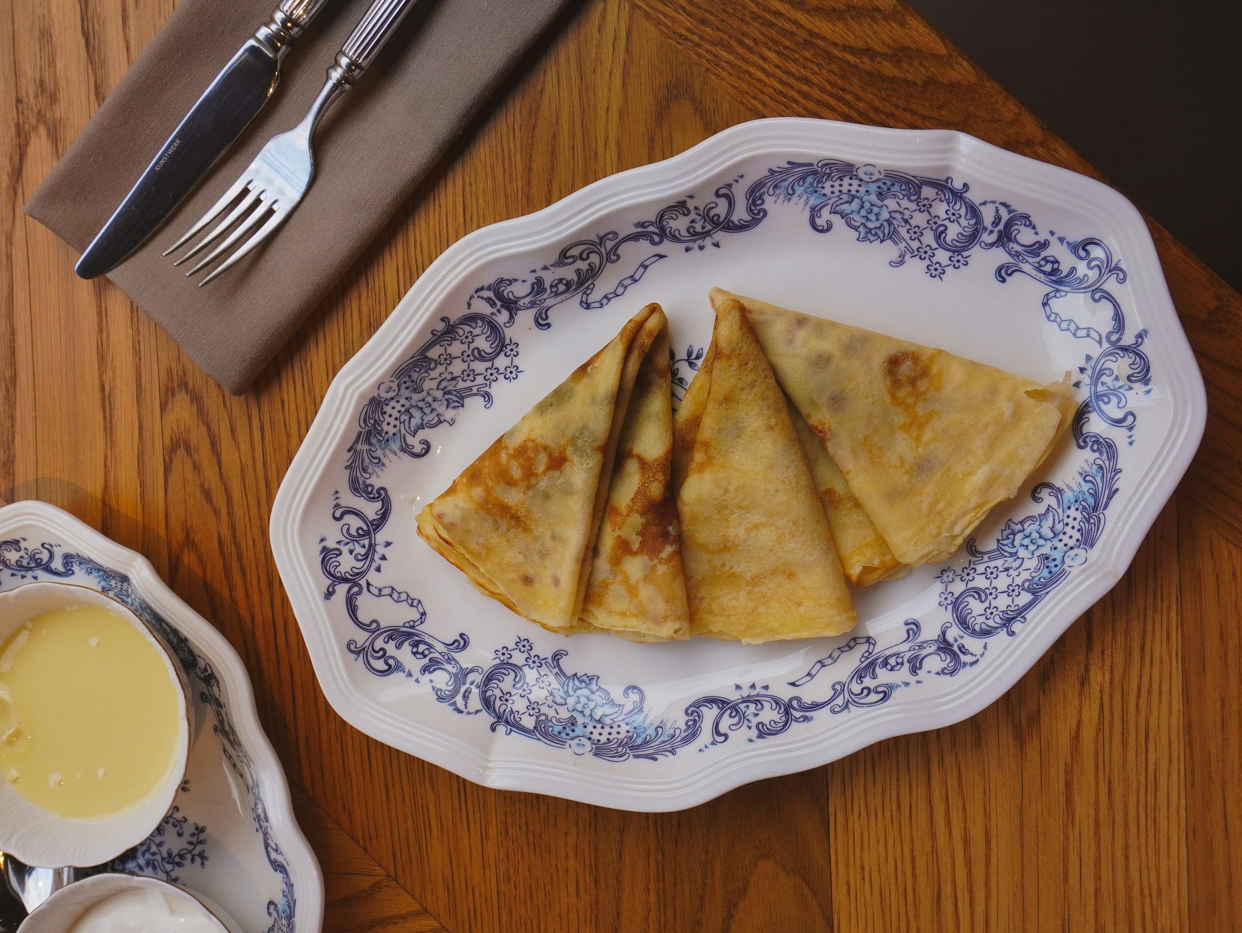 Tasty crepes beautifully plated on ornate porcelain with syrup and cutlery.