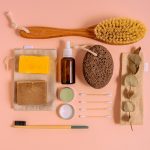 Flat lay of natural bath products including soaps, brush, and pumice on a peach surface.
