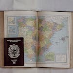 Open vintage atlas showing Spain and Portugal with a Venezuelan passport on top, symbolizing travel.