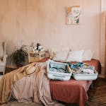 Open suitcase on a bed in a cozy, warmly decorated bedroom, ready for travel.