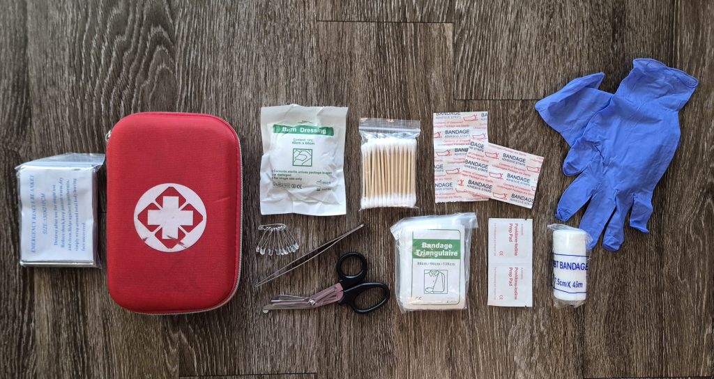 first aid kit with emergency blanket, safety pins, scissors, tweezers, bandages, gloves, and cleansing wipes